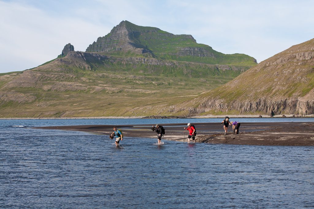 Wandergruppe in Island läuft barfuß durch einen breiten Bach